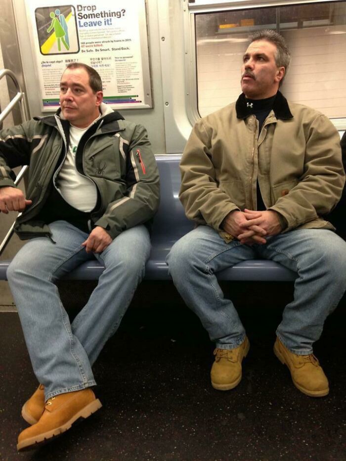 Two men dressed similarly, sitting confidently on a subway, appearing to blend in effortlessly.