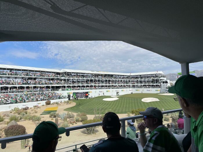 People blending in at a golf tournament, overlooking a crowded stadium and green.