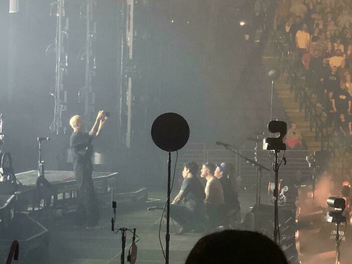 Stage scene with people pretending to belong, taking photos at a concert, capturing moments by the stage.