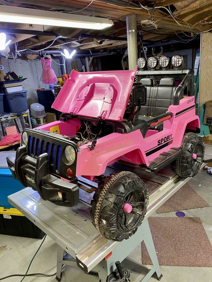 Pink toy car being repaired in a basement workshop, capturing a funny and goofy dad moment.