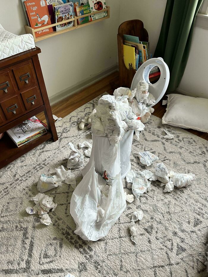 Overflowing trash can with scattered diapers on a rug in a child's room, capturing a funny dad moment.