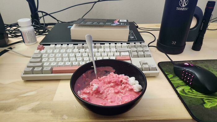 Bowl of pink, unconventional dish on desk with keyboard, book, and mug, representing strange food ideas.