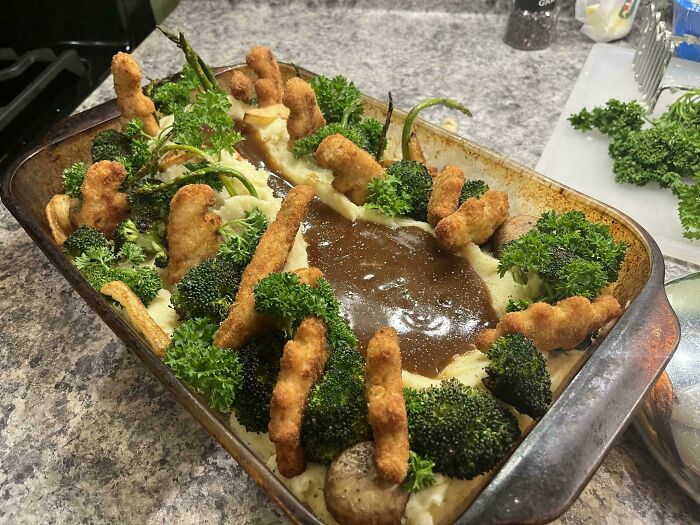Unusual dish with chicken strips, broccoli, and gravy in a baking dish, arranged in an eccentric presentation.