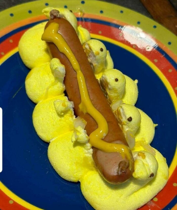 Hotdog with marshmallow chicks covered in mustard on a colorful plate.