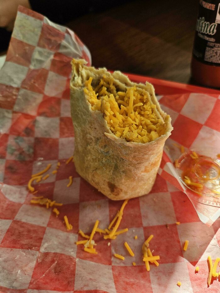 Burrito filled solely with shredded cheese on a red-checkered paper.