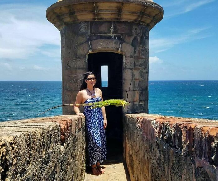 Woman standing by a stone tower near the ocean with a large iguana appearing to float in front, capturing a wild coincidence.