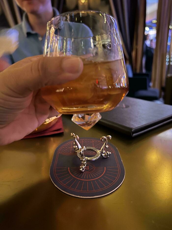 Hand holding an unusual cocktail glass with a diamond-shaped base in a restaurant with ridiculous food serving style.