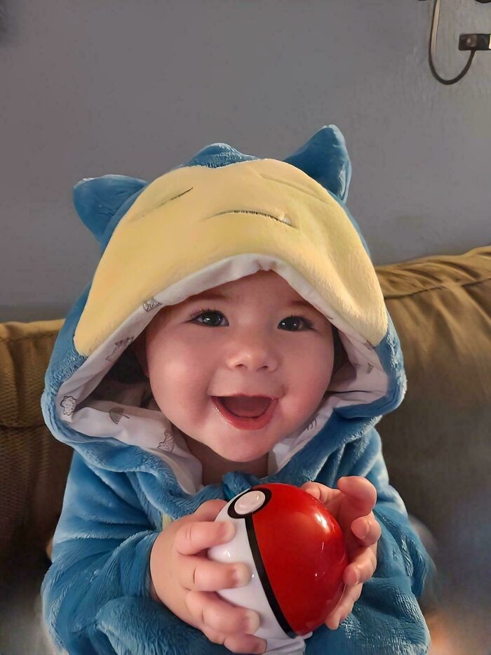 Smiling baby in a Snorlax costume holding a Pokeball, capturing a wholesome and funny dad moment.