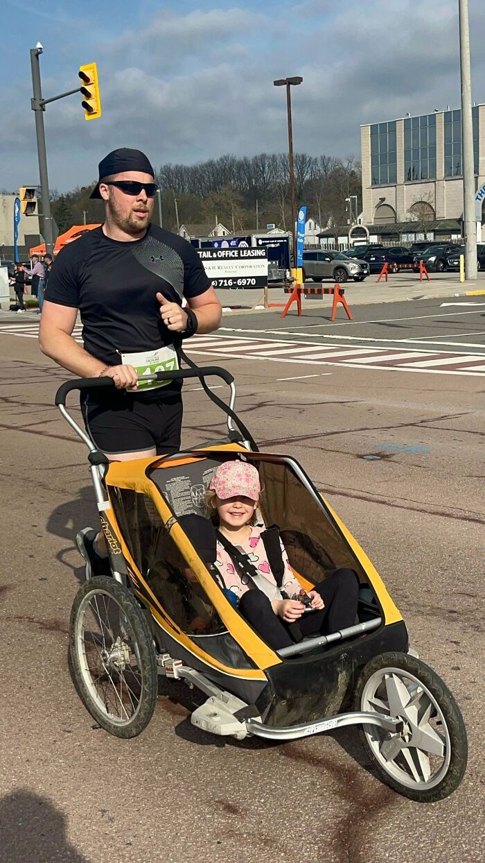 Man running outside pushing a stroller with a young child smiling inside, capturing a wholesome dad moment.