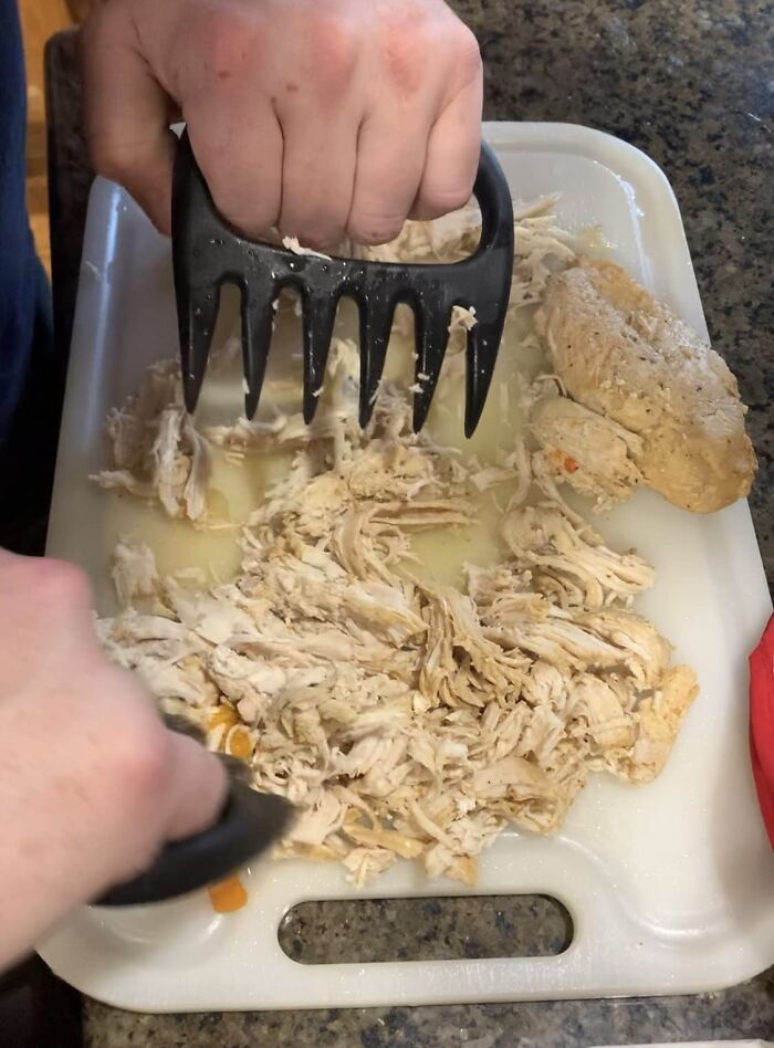 Hands using meat shredder claws to pull apart cooked chicken on a cutting board from popular Amazon finds.