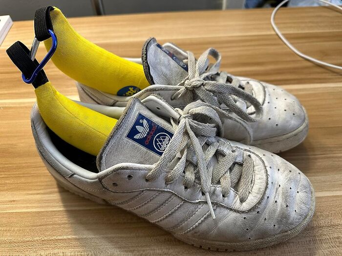 White Adidas sneakers with yellow banana-shaped shoe inserts and blue carabiner clips on a wooden surface, Amazon finds.