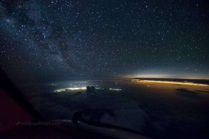 Aerial night sky view from pilot’s perspective showing stars, clouds, and city lights on the horizon in breathtaking detail