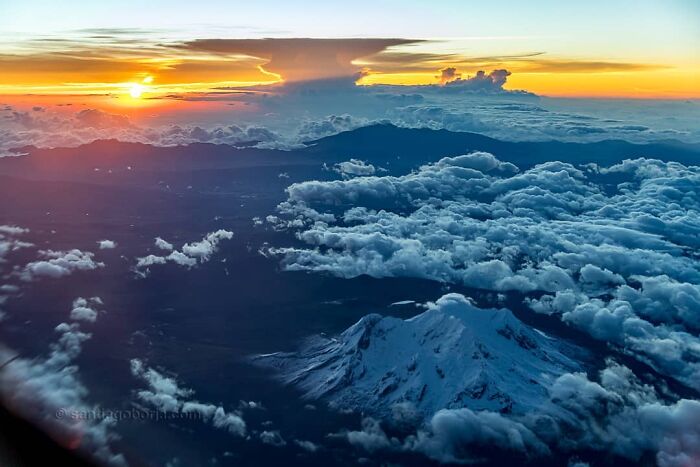 Aerial view of snow-capped mountains and clouds during a colorful sunset captured by a pilot from high altitude.