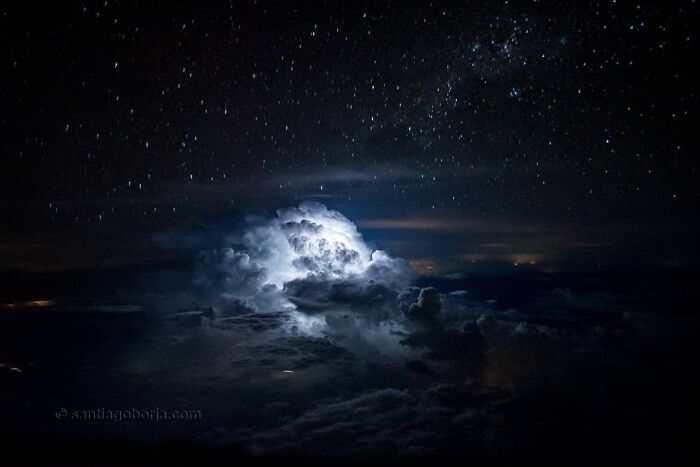 Breathtaking aerial photo of a storm cloud illuminated at night, captured from above under a starry sky by a pilot.