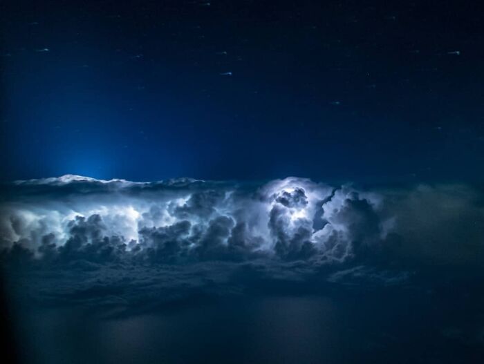 Aerial photo of glowing storm clouds at night captured by a pilot showing dramatic lighting and deep blue sky.