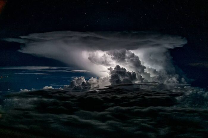 Dramatic aerial photo of a glowing thunderstorm cloud illuminated against a dark night sky captured by pilot.