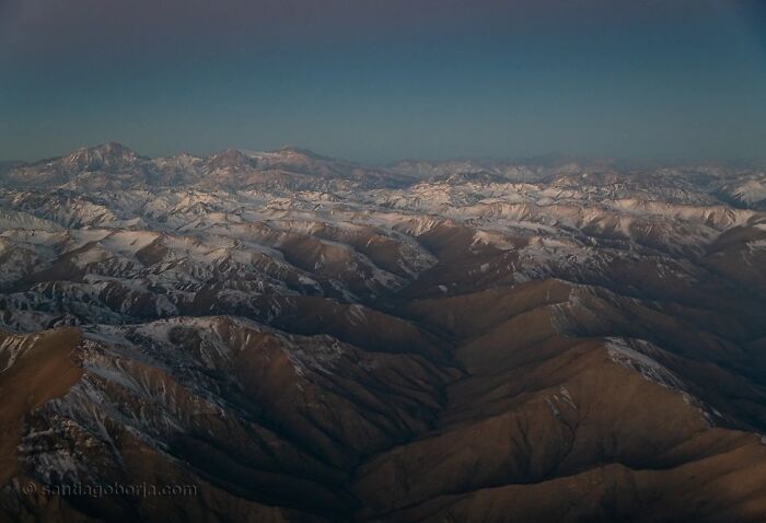 Aerial view of a vast mountain range with snow patches under a clear sky captured in breathtaking aerial photos.