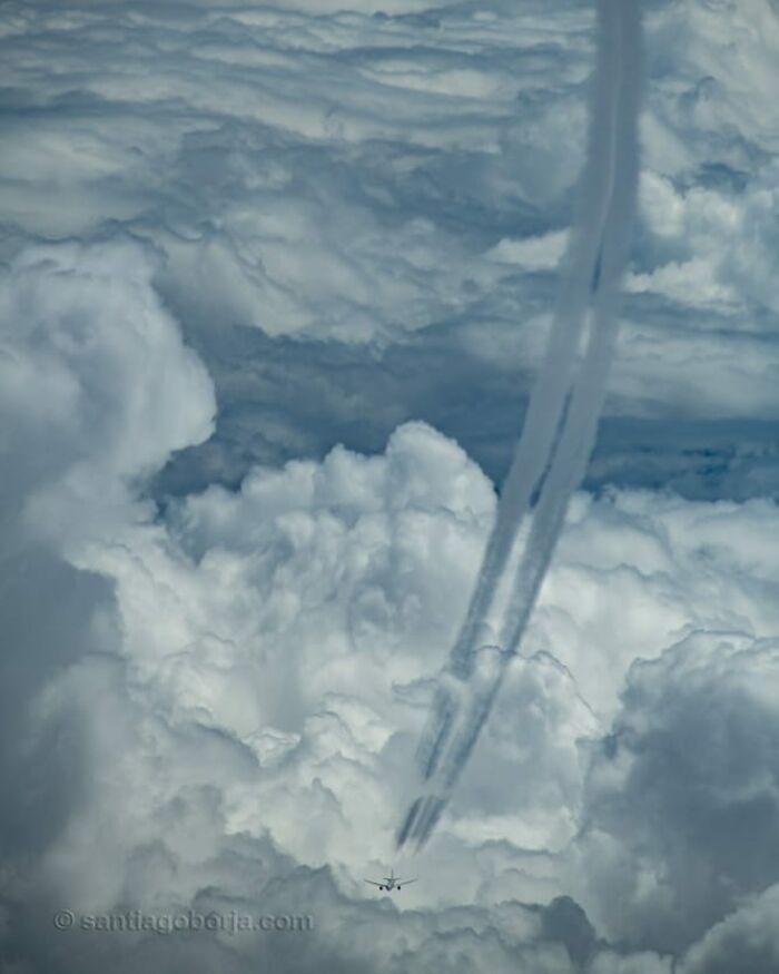 Aerial photo of a plane flying above thick clouds, leaving dramatic contrails in a breathtaking sky scene.