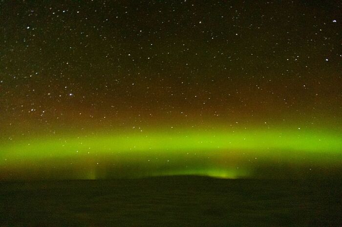 Northern lights glowing bright above a dark landscape captured in breathtaking aerial photos by this pilot at night.