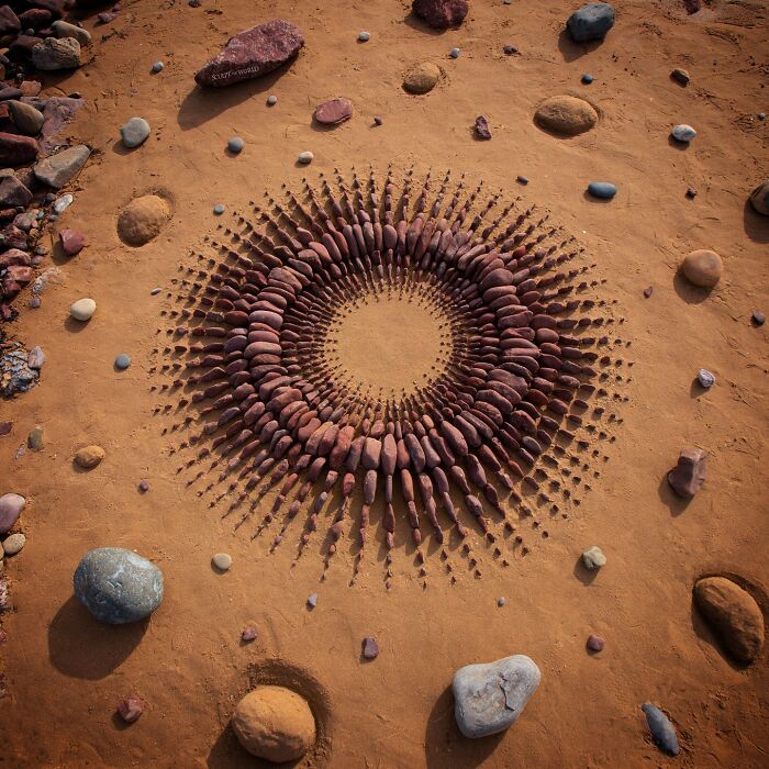 Circular land art made with natural stones arranged patiently on sandy ground in a detailed pattern by an artist.
