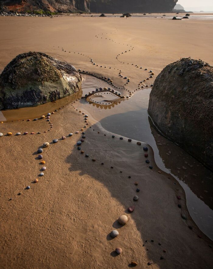 Curved patterns made with small stones between rocks on a sandy beach, example of patience-requiring land art with natural materials.
