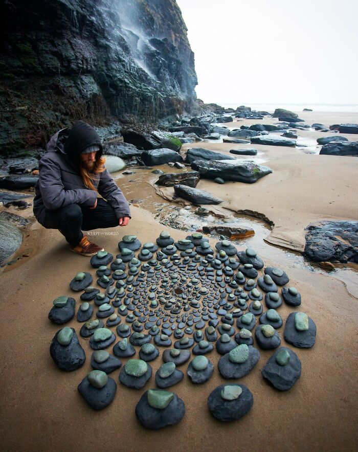 Artist creating a patience-requiring land art piece on a sandy beach using natural materials like stones arranged in a spiral pattern.