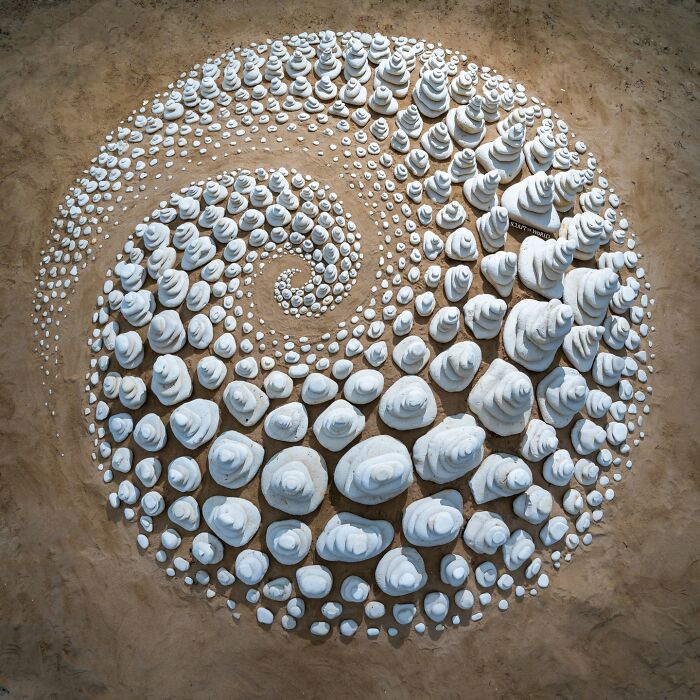 Spiral land art piece created with natural stones arranged meticulously requiring great patience by the artist on sandy ground.