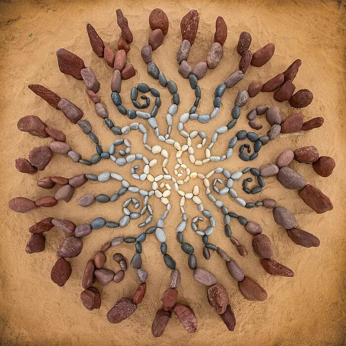 Intricate land art piece made with natural stones arranged in a radial, spiral pattern on sandy ground requiring great patience.