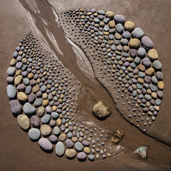 Circular land art on sand featuring arranged natural stones forming a detailed pattern requiring patience and precision.