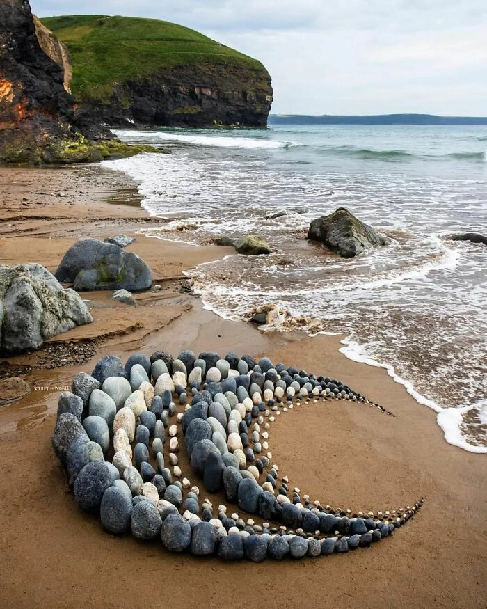 Curved land art piece made of natural stones on a beach near waves and cliffs, showcasing patience-requiring craftsmanship.