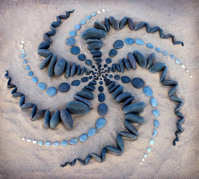 Spiraling land art made with natural stones arranged meticulously on sand, showcasing patience-requiring natural material design.