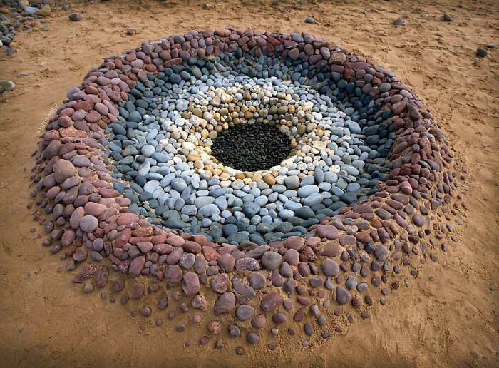 Concentric land art piece made with natural stones arranged meticulously on sandy ground by the artist.