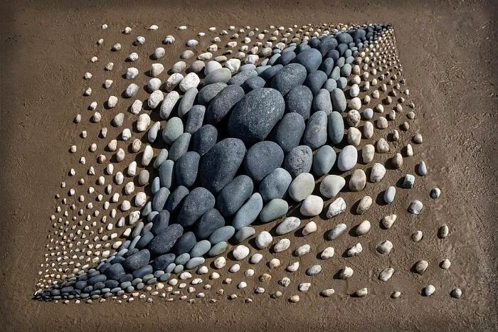 Land art piece made with natural stones arranged in a 3D pattern, showcasing patience and intricate design by the artist.