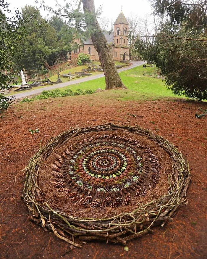 Intricate land art piece made with natural materials, featuring pinecones and twigs arranged in concentric circles outdoors.