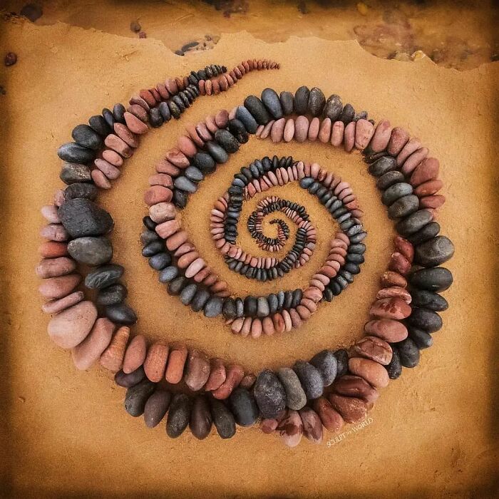 Spiral land art piece made with natural stones arranged patiently in concentric circles on sandy ground.