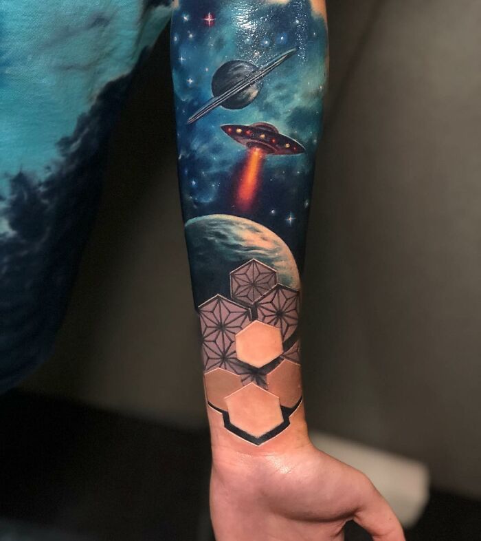 Tattoo of a cosmic scene with planets, UFO, and geometric shapes on a forearm, showcasing a world within the skin.