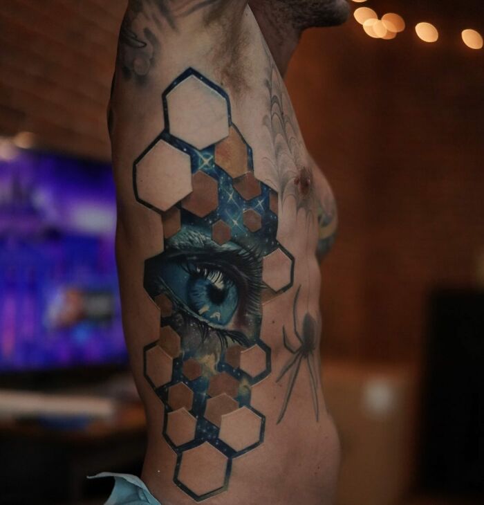 Intricate tattoo featuring an eye and geometric shapes on a person's side, showcasing skin artistry.