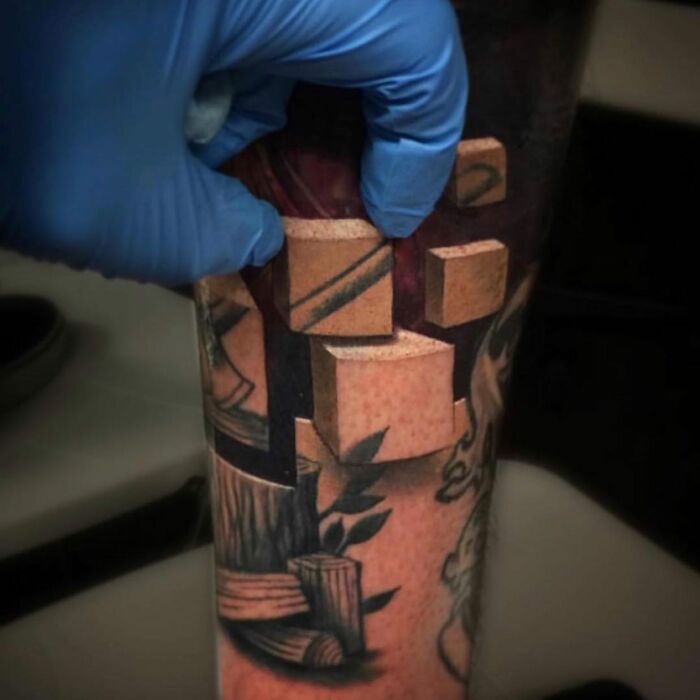 Tattoo with 3D cubes on skin, one being pinched by a gloved hand, illustrating a world within the skin.