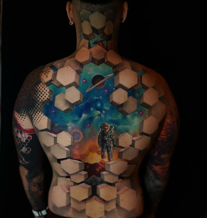 Back tattoo with hexagonal patterns, depicting an astronaut and cosmic scene, showcasing a world within the skin.