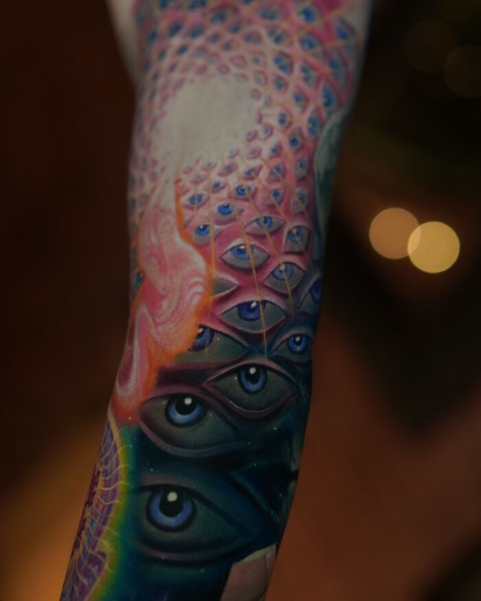 Abstract tattoo with intricate eye pattern and pink geometric design, showcasing a world within the skin.