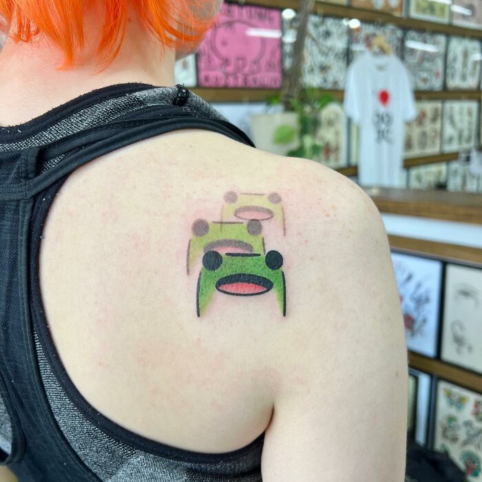 Tattoo on a person's shoulder featuring colorful abstract faces, designed by Buoy.
