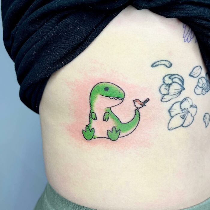 Charming tattoo by Buoy featuring a cute dinosaur with a bird on its tail.