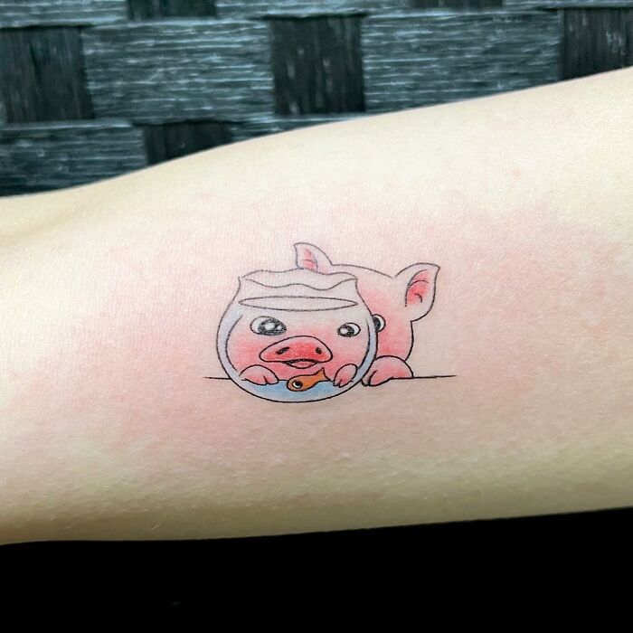 Charming tattoo of a cartoon pig peeking from behind a fishbowl on an arm.