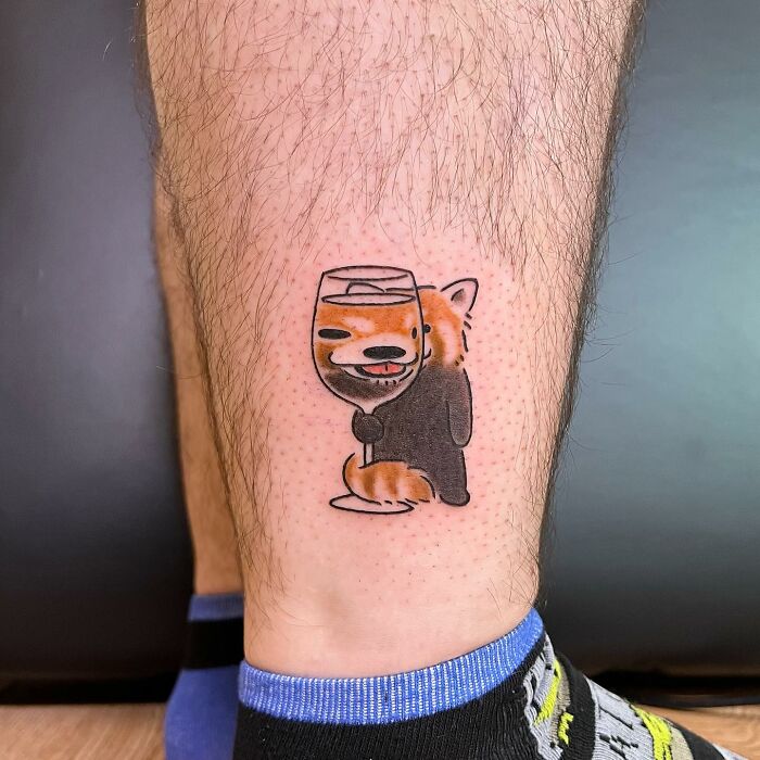 Charming tattoo of a cute fox holding a wine glass on a person's leg.