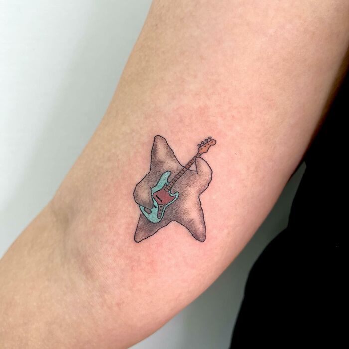 Tattoo of a teal guitar on an arm by Buoy, showcasing charming artistic style.