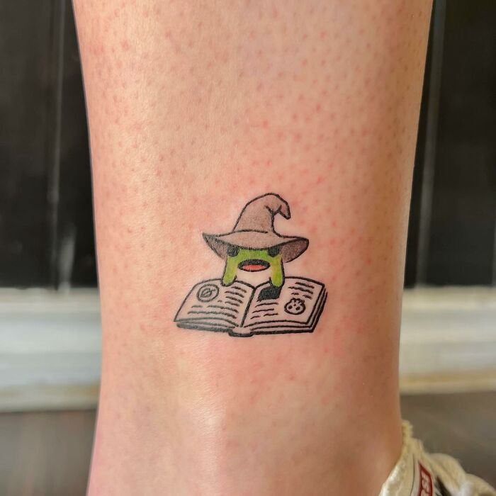 Tattoo of a small green wizard with a hat reading a book on skin.