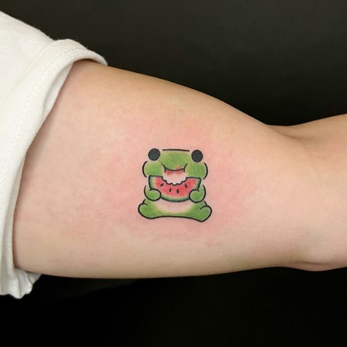 Charming tattoo of a frog eating watermelon on an arm, by artist Buoy.