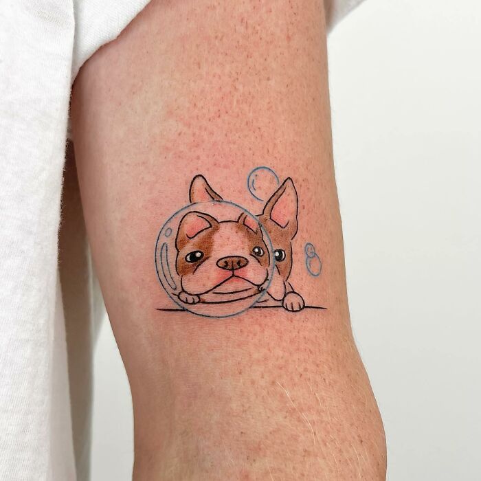 Cute dog tattoo by Buoy on an arm, featuring a French Bulldog in a bubble with a playful expression.