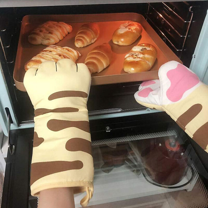 Whimsical animal oven mitts holding a baking tray with fresh bread rolls.