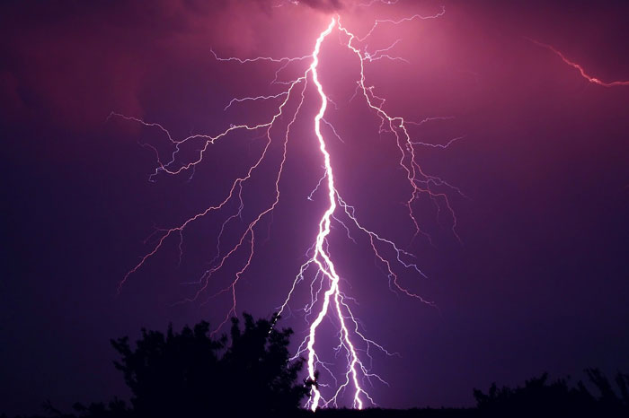 Bright lightning bolt in a night sky indicating a thunderstorm, natural phenomenon that can scare dogs.